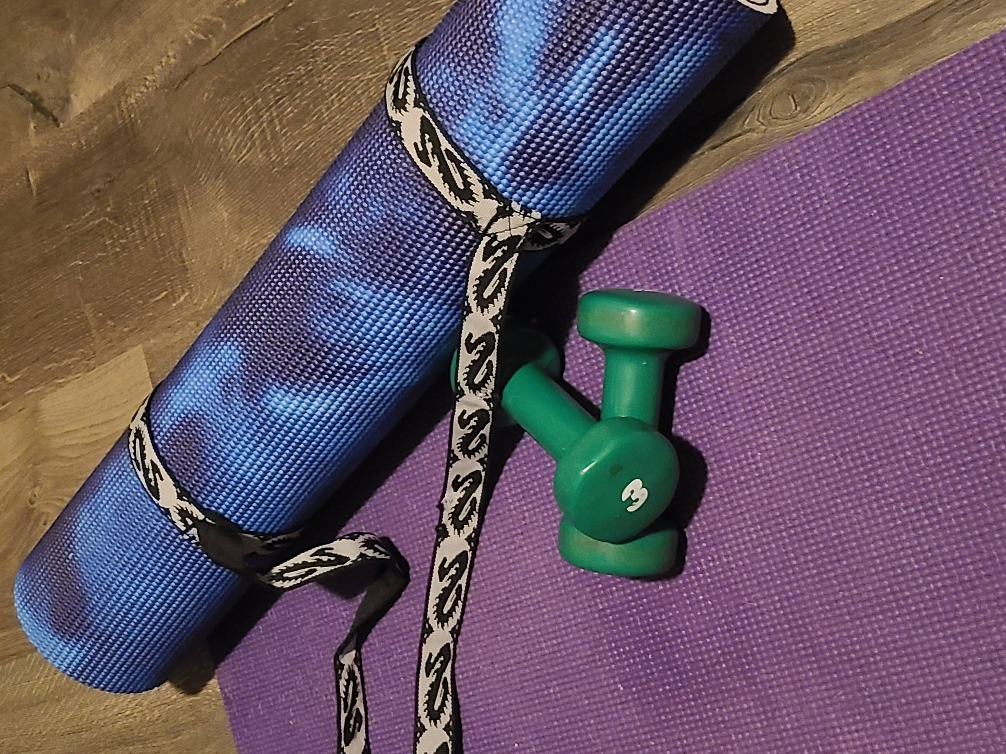 A rolled yoga mat sitting beside two green hand weights on an opened yoga mat